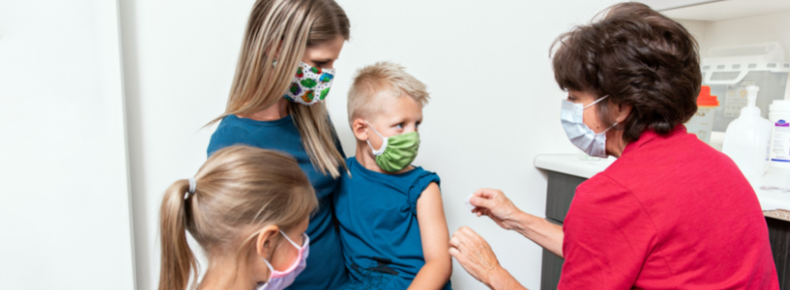 Child getting vaccinated by nurse with mom and sibling there too