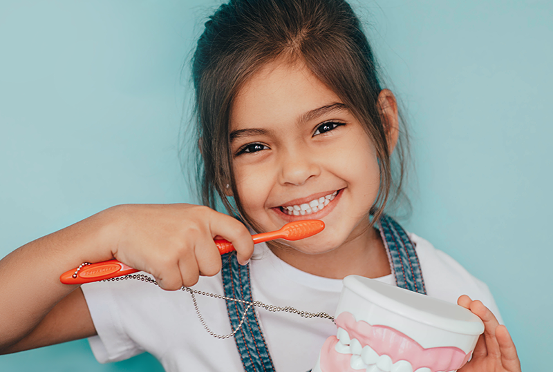 Photo of a happy young girl brushing her teeth.