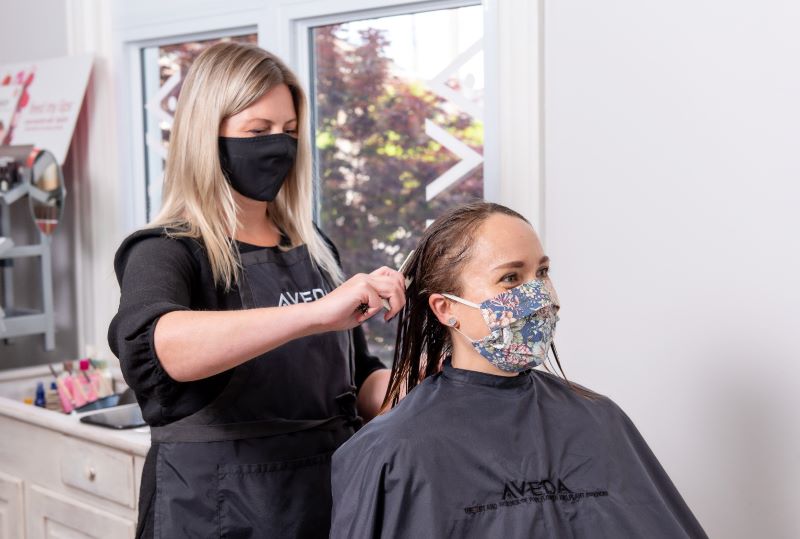 hair stylist wearing a mask cutting a clients hair