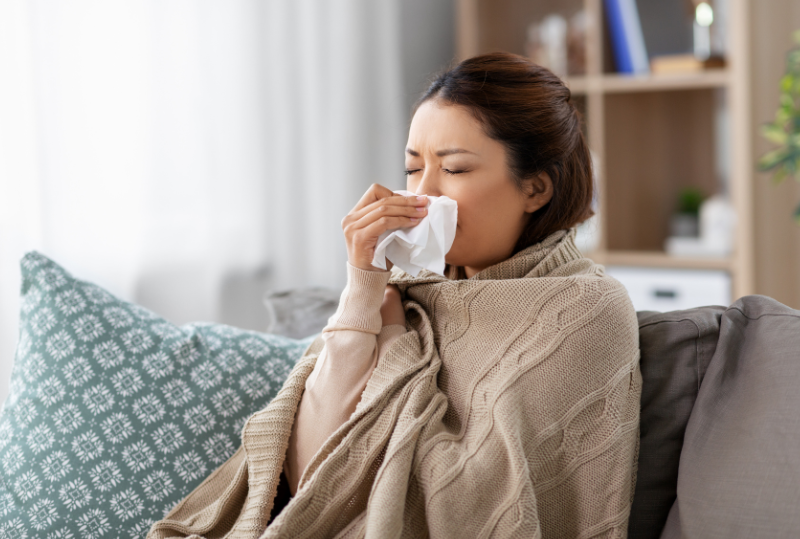 Photo of a woman wrapped in blankets and blowing her nose
