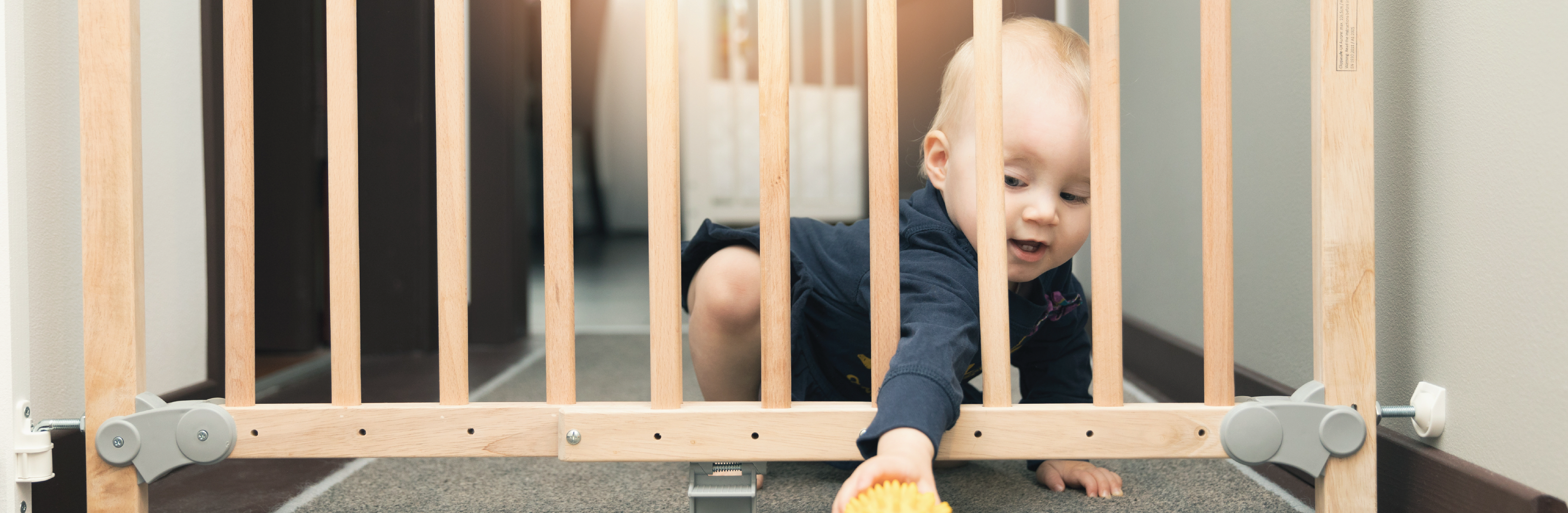 toddler reaching through baby gate at the top of stairs