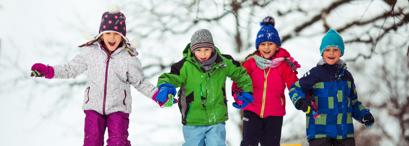 group of 4 children in bright coloured snowsuits walking in the snow