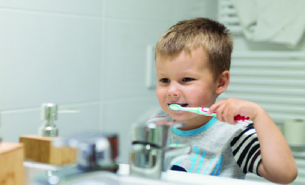 Young boy brushing his teeth in the bathroom mirror