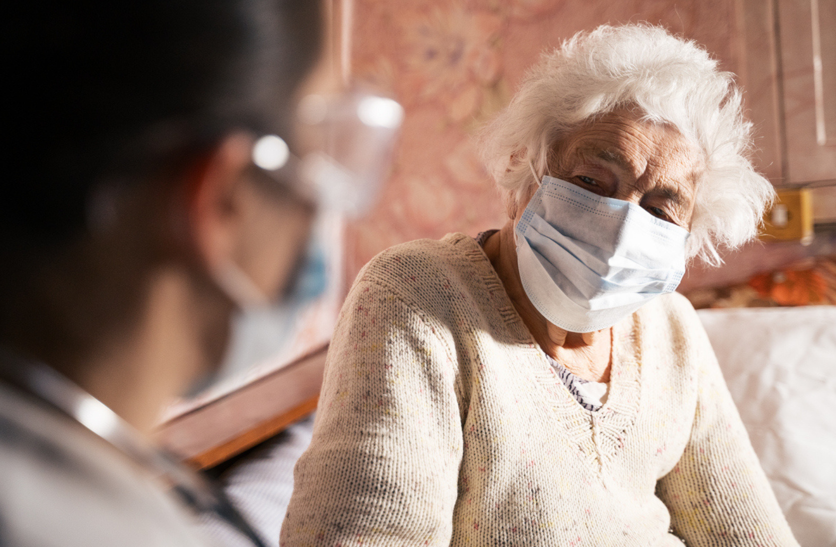 Picture of an elderly woman with a mask talking to care provider