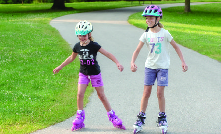 Two young girl rollerblading down path with helmets on
