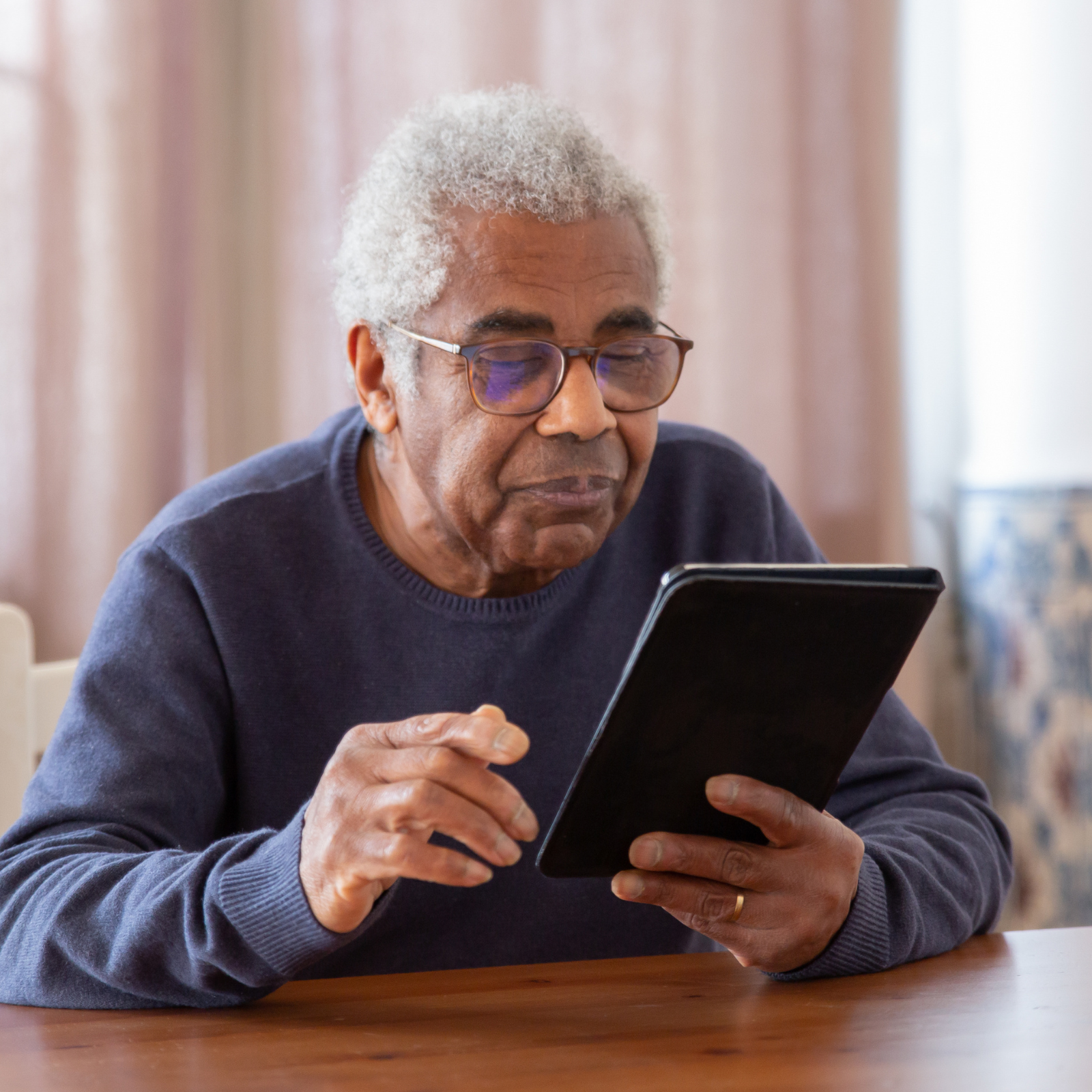 Older man wearing glasses using a tablet at home