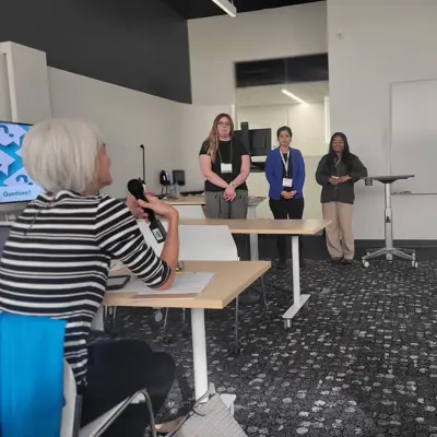 Three women standing in front of a classroom while an audience member holds a microphone