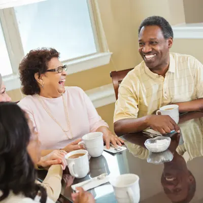 Group of older adults laughing together around a dining table with coffee mugs