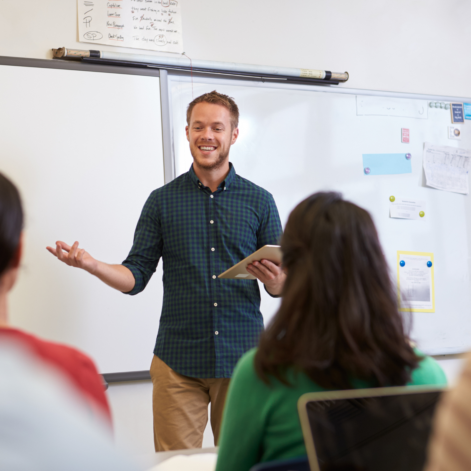 Male teacher speaking in front of a whiteboard while holding a tablet