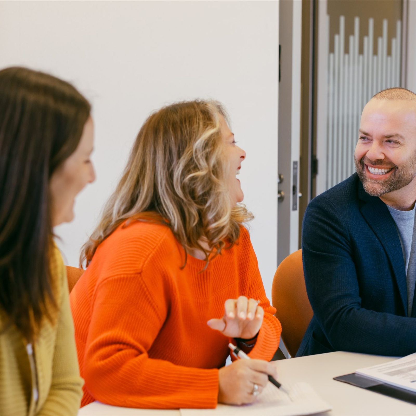 Three colleagues sitting at a meeting table, laughing and having a lively discussion