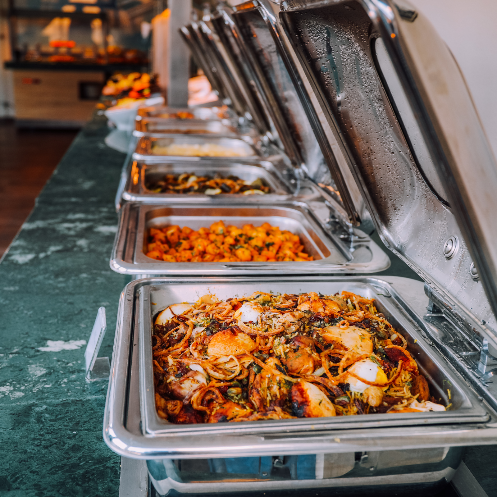 Open buffet with hot food trays filled with various dishes in a commercial food service setting
