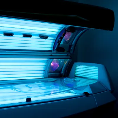 Open tanning bed glowing with blue light in a dark room