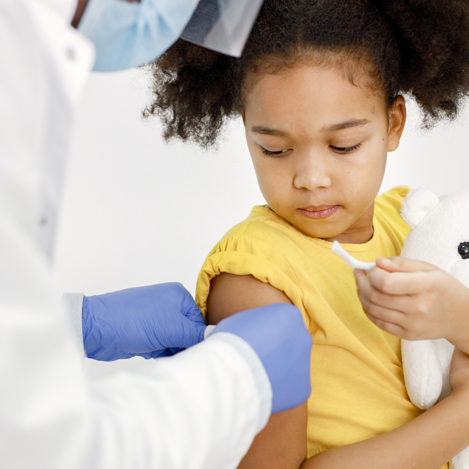 Young girl holding a stuffed animal while receiving a vaccine in her arm