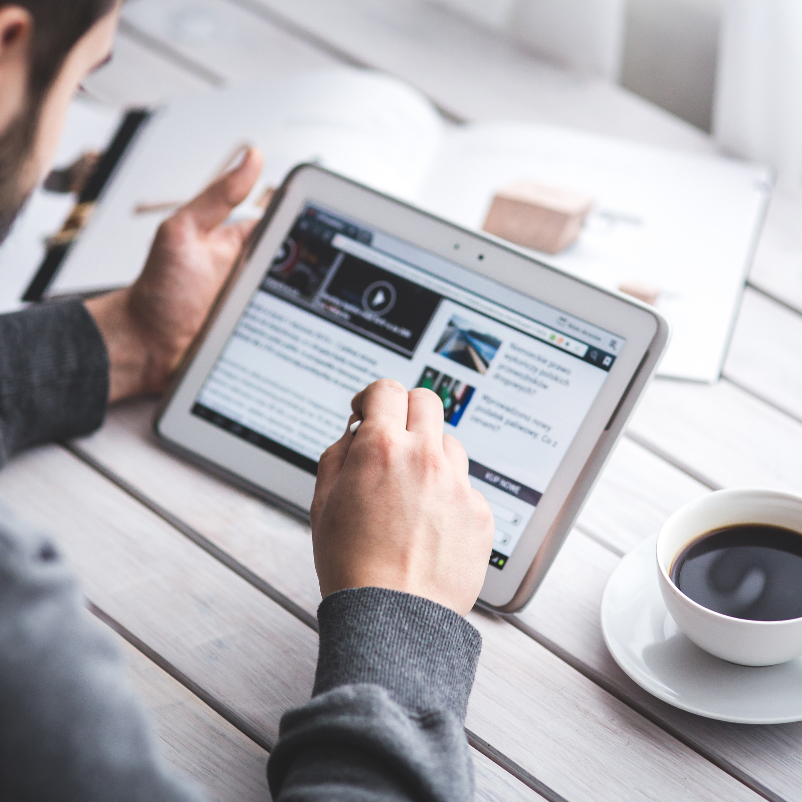 Person reading online news on a tablet next to a cup of coffee