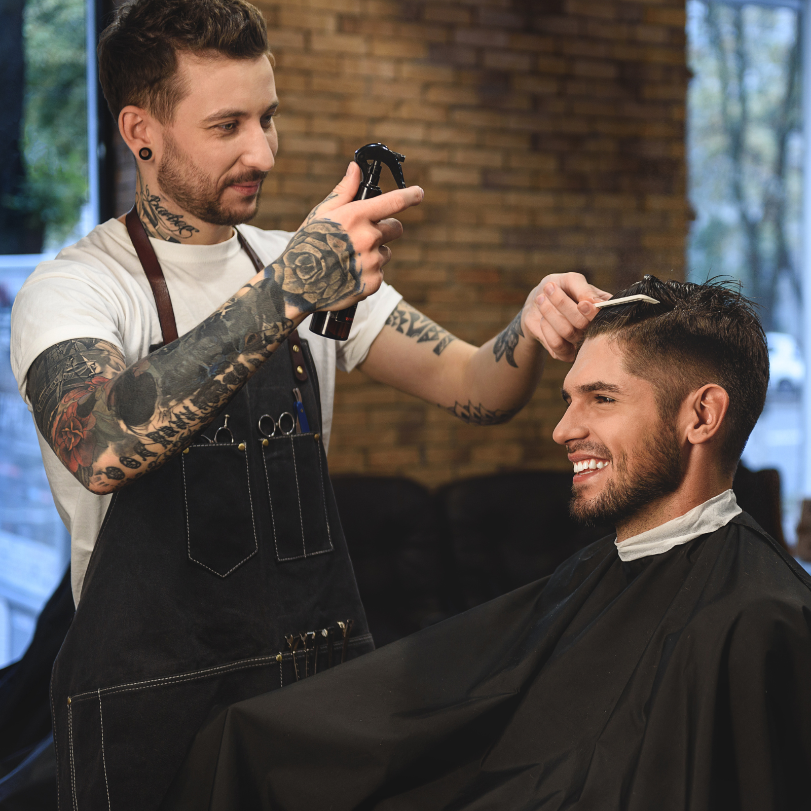 Tattooed barber smiling while giving a haircut to a male client in a salon