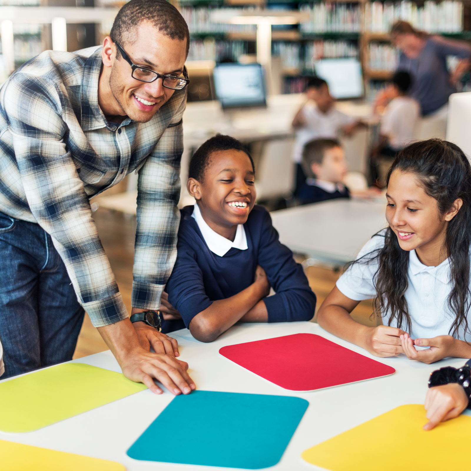 Teacher laughing with students around a colourful table in a classroom setting