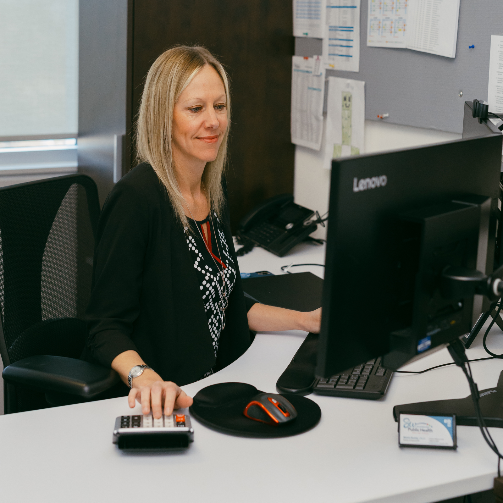 Woman using a calculator at a desk with a computer monitor and phone
